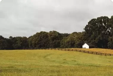 Open grassy field with trees and a white barn, representing inherited land sold to Landacy